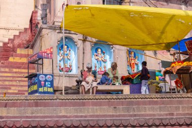 Varanasi, Uttar Pradesh, Hindistan - 22 Mart 2024: Varanasi 'deki çetelerin yakınındaki assi ghat' ta şemsiye altında oturan geleneksel bir Brahman rahibinin portresi.