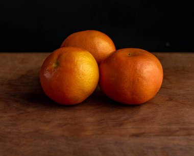 Ahşap bir masada siyah arka planı olan üç Mandarin portakalı.