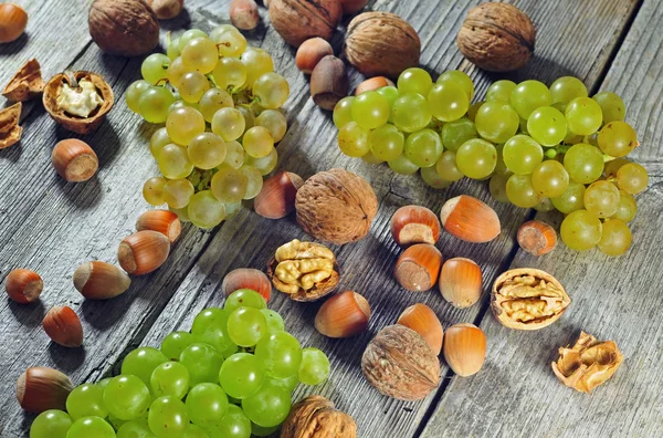 Uvas, avelãs e nozes numa mesa de madeira — Fotografia de Stock