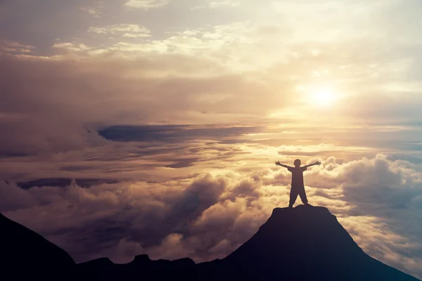 Bulutların üstünde dağın tepesinde duran bir çocuk. Succ