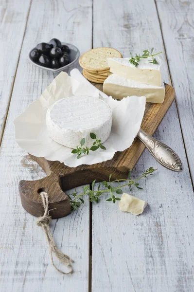 Queso Brie con galletas y aceitunas en la mesa de madera blanca —  Fotos de Stock