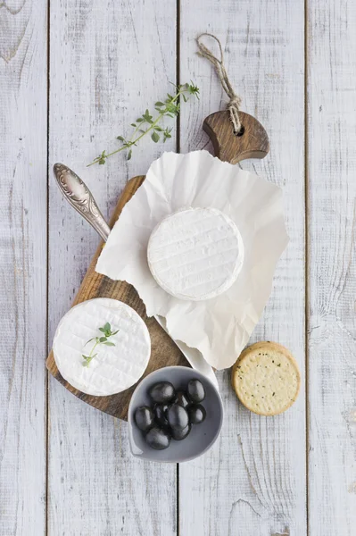 Queso Brie con galletas y aceitunas en la mesa de madera blanca —  Fotos de Stock