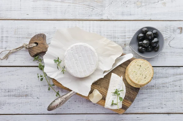 Queso Brie con galletas y aceitunas en la mesa de madera blanca —  Fotos de Stock