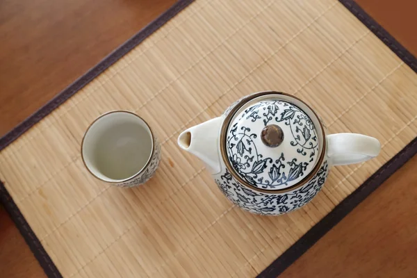 Chinaware blue and white porcelain teapot and empty cup on bamboo tablemat. — Stock Photo, Image