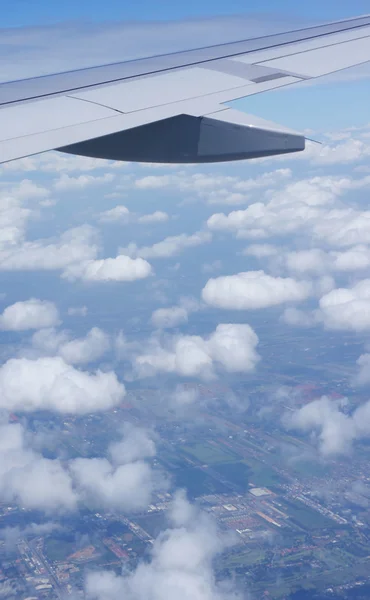 Jet uçağın kanat ve beyaz bulutlar görmek, aşağıda arazi. — Stok fotoğraf