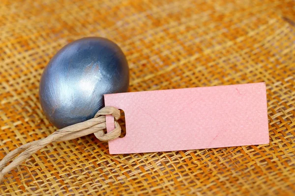 Uovo di Pasqua e etichetta di carta bianca su sfondo foglio di tessitura di bambù . — Foto Stock