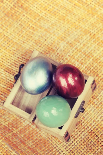 Ovos de páscoa coloridos em pequena caixa de madeira em folha de tecido de bambu . — Fotografia de Stock