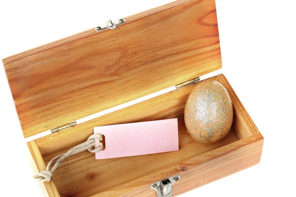 Золотое пасхальное яйцо и бумажная бирка в деревянной коробке на белой спинке — стоковое фото
