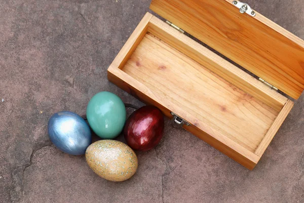 Colorful easter eggs and wooden box on stone floor. — Stock Photo, Image