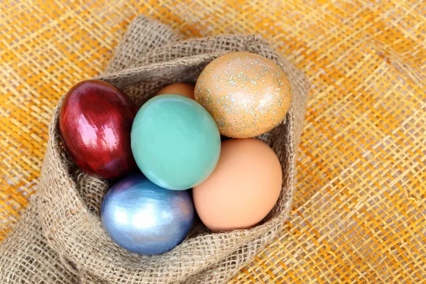 Colorful easter eggs in sack bag on weave background. — Stock Photo, Image