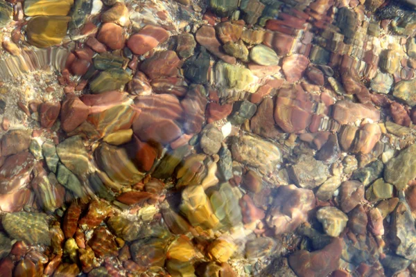 Pebbles coloridos borrados na praia com textura de água . Fotografia De Stock