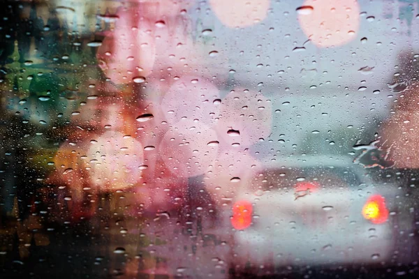 Driving in rain, raindrops on car window with light bokeh, rainy season.