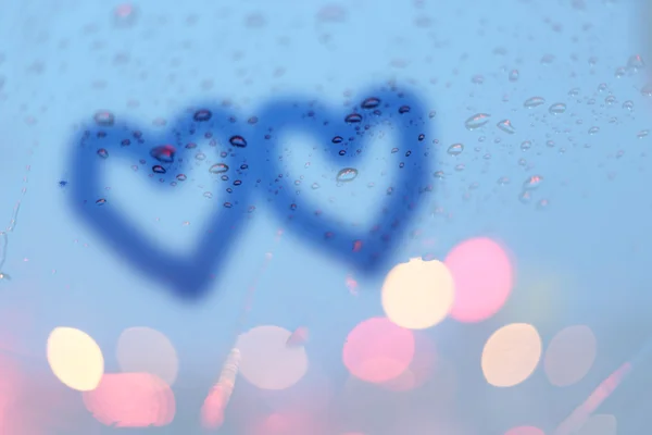Krople deszczu i dwa serca pisać na okno z światła bokeh, deszcz — Zdjęcie stockowe