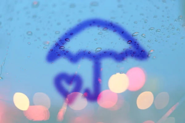 Gotas de chuva e guarda-chuva e coração escrever na janela com luz bok — Fotografia de Stock