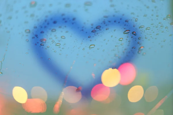Krople deszczu i niewyraźne serce pisać na okno z światła bokeh, r — Zdjęcie stockowe