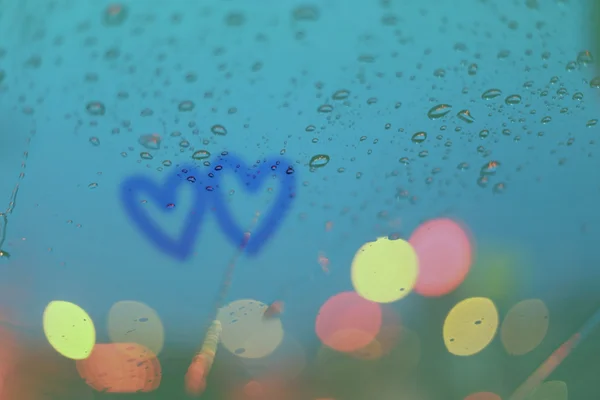 Gotas de chuva e dois corações escrevem na janela com luz bokeh, chuva — Fotografia de Stock