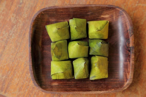 Thai dessert wrapped in banana leaves on wooden dish. — Stock Photo, Image