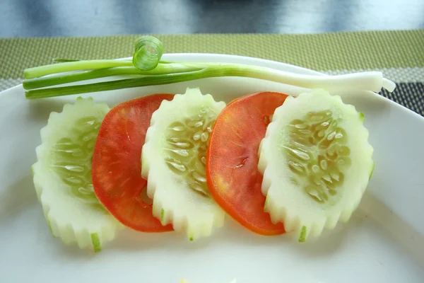 Schalottenlök, skivor av gurkor och tomater på kanten av vita plat — Stockfoto
