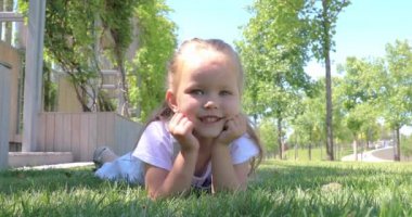 Yakından gülümseyen küçük tatlı bir kız çocuğu yeşil çimlerin üzerinde yatıyor. Küçük güzel bir kız kameraya gülümsüyor. Mutlu çocukluk