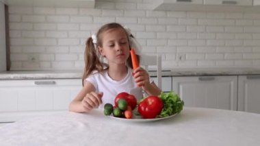 Çocuk neşeyle sebze yiyor. Küçük kız mutfakta havuç yiyor. Sağlıklı beslenme kavramı