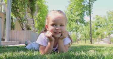 Yakından gülümseyen küçük tatlı bir kız çocuğu yeşil çimlerin üzerinde yatıyor. Küçük güzel bir kız kameraya gülümsüyor. çocukluk