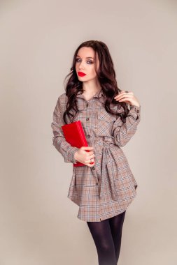 Kırmızı dudaklı güzel bir genç kız elinde kırmızı bir defter tutuyor. Öğrenci. İzole edilmiş gri arka planda bir iş kadını. Uzayı kopyala dikey resim