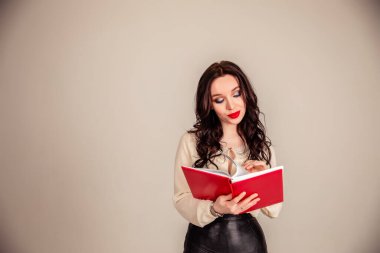 Kırmızı dudaklı güzel bir genç kız elinde kırmızı bir defter tutuyor. Gri arka planı olan bir öğrenci. Eğitim. Boşluğu kopyala
