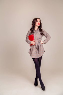 Kırmızı dudaklı güzel bir genç kız elinde kırmızı bir defter tutuyor. Öğrenci. İzole edilmiş gri arka planda bir iş kadını. Uzayı kopyala dikey resim