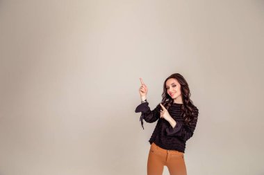 Çekici, hayret verici, stil sahibi, etkilenmiş, komik bir kızın gri arka planda izole edilmiş boş bir yeri işaret eden bir portresi.