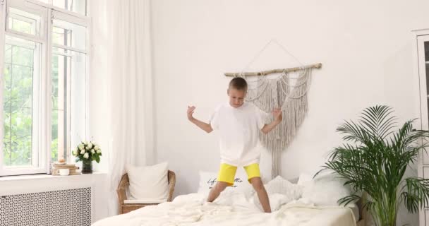 Een jongen in een wit T-shirt dansend op een bed. 8-10 jaar — Stockvideo