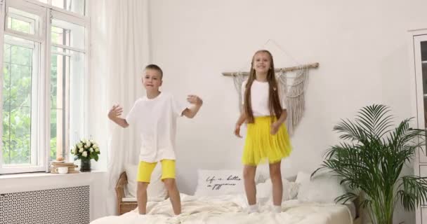 Un garçon et une fille en T-shirts blancs dansent et sautent sur le lit. frère et sœur. bonne enfance. enfants rouges — Video