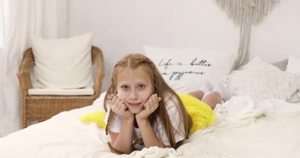 Portret van een tiener rood meisje. het meisje ligt op het bed en kijkt naar de camera — Stockvideo