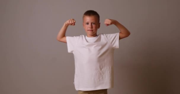 O menino mostra seus músculos em seus braços. Rapaz forte. criança em uma camiseta branca — Vídeo de Stock