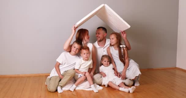 Szczęśliwa Duża Rodzina Siedzi Pod Kartonowym Dachem Domu Koncepcja Ubezpieczenia — Wideo stockowe