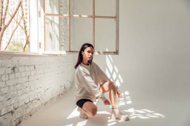 Spor kıyafetli güzel esmer kız büyük bir pencerenin yanında yerde oturuyor.