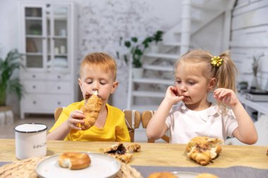Küçük bir oğlan ve küçük bir kız kruvasan yiyorlar. Çocuklar çikolataya bulandılar. Ağabey ve abla kahvaltı yapıyor.