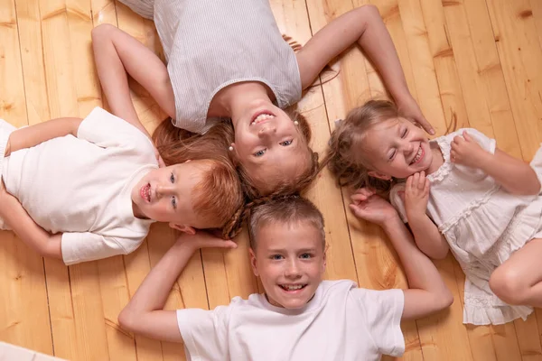 portrait of brothers and sisters.. four children lie on the floor and looking at camera. red children