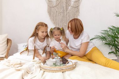 Anne ve kızları yatakta kahvaltı yapıyor.