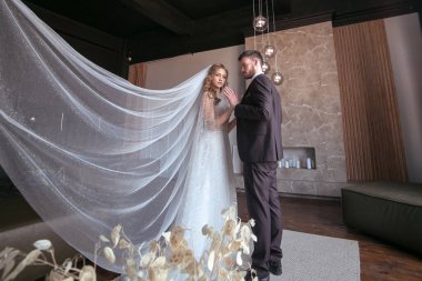Güzel bir çift. Gelin, uzun beyaz peçeli ve gelinlikli. Şık takım elbiseli bir damat. karanlık iç mekan