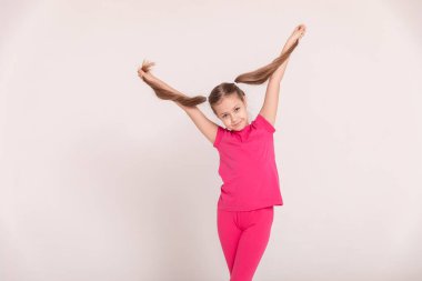 Beyaz arka planda mutlu bir çocuk. Pembe tişörtlü ve pantolonlu bir kız. Kuyruklu kız. Boşluğu kopyala