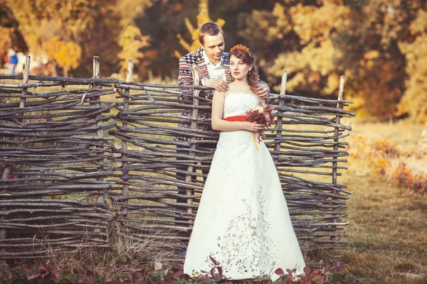 Newlyweds standing near the wicker fence — Stock Photo, Image