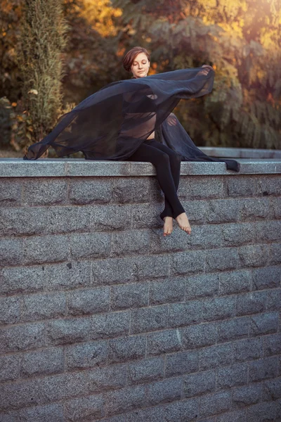 Dziewczyna tancerz z czarny szal siadając na kamiennym murem — Zdjęcie stockowe
