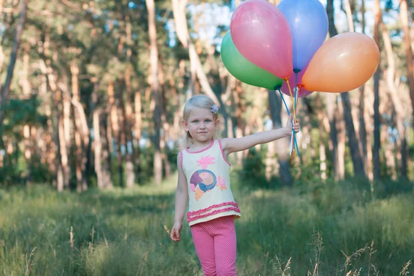 Menina com um braço cheio de balões na floresta — Fotografia de Stock