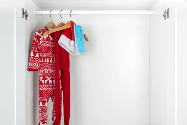 白色和红色的圣诞睡衣 紧身衣和面罩挂在白色衣橱里的木制衣架上的横向彩色图像 验尸官大流行病期间的休假 — 图库照片