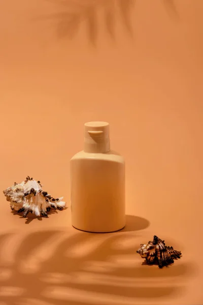 Bej arka planda bir şişe güneş kremi ve tropikal yaprakların gölgeleri. Cilt bakımı ve koruma konsepti. Altın ten..
