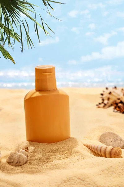 Kumsalda bir şişe güneş kremi. Cilt bakımı ve koruma konsepti. Altın ten..
