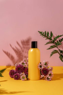 Çiçekli sarı ve pembe arka planda kozmetik ürünleri için yaz gösterisi. Çiçekli sarı şişe kozmetik ürünleri