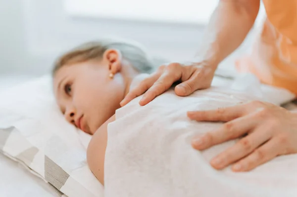 real doctor osteopath hands does physiological and emotional therapy for eight year old kid girl. pediatric osteopathy treatment session. alternative medicine. taking care of the child\'s health