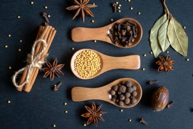 Tahta kaşıklar ve farklı yüzeylerdeki çeşitli baharatlar..