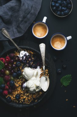Sağlıklı kahvaltı. Yulaf granola kek taze meyveler, tohumlar ve demir tava tava koyu ahşap tahta üzerinde siyah zemin üzerinde kahve dondurma